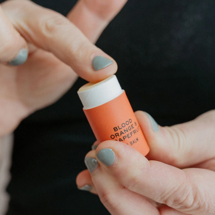 hand holding lip balm while finger touches top of balm