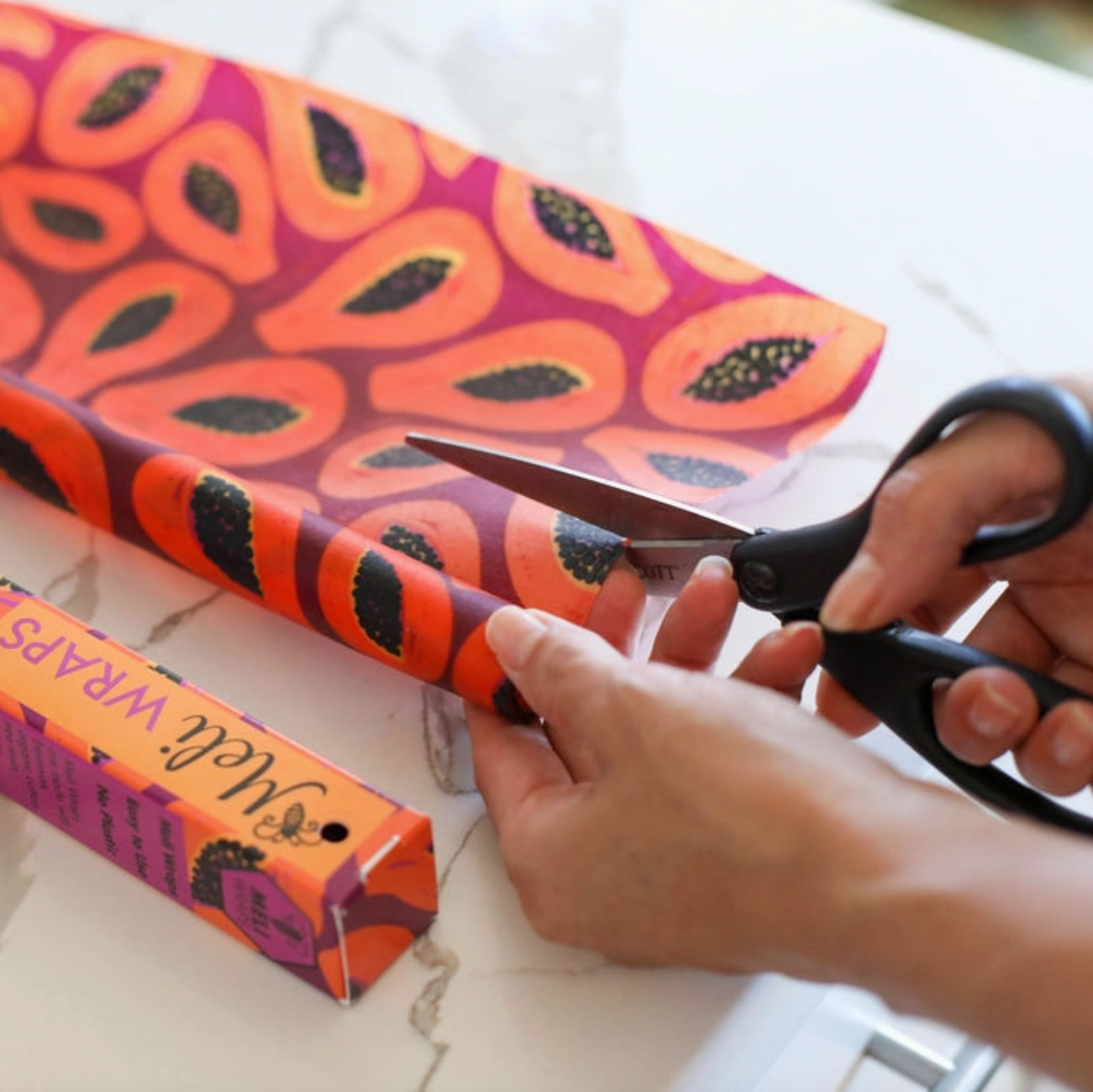Person cutting a colorful box with scissors on a white surface