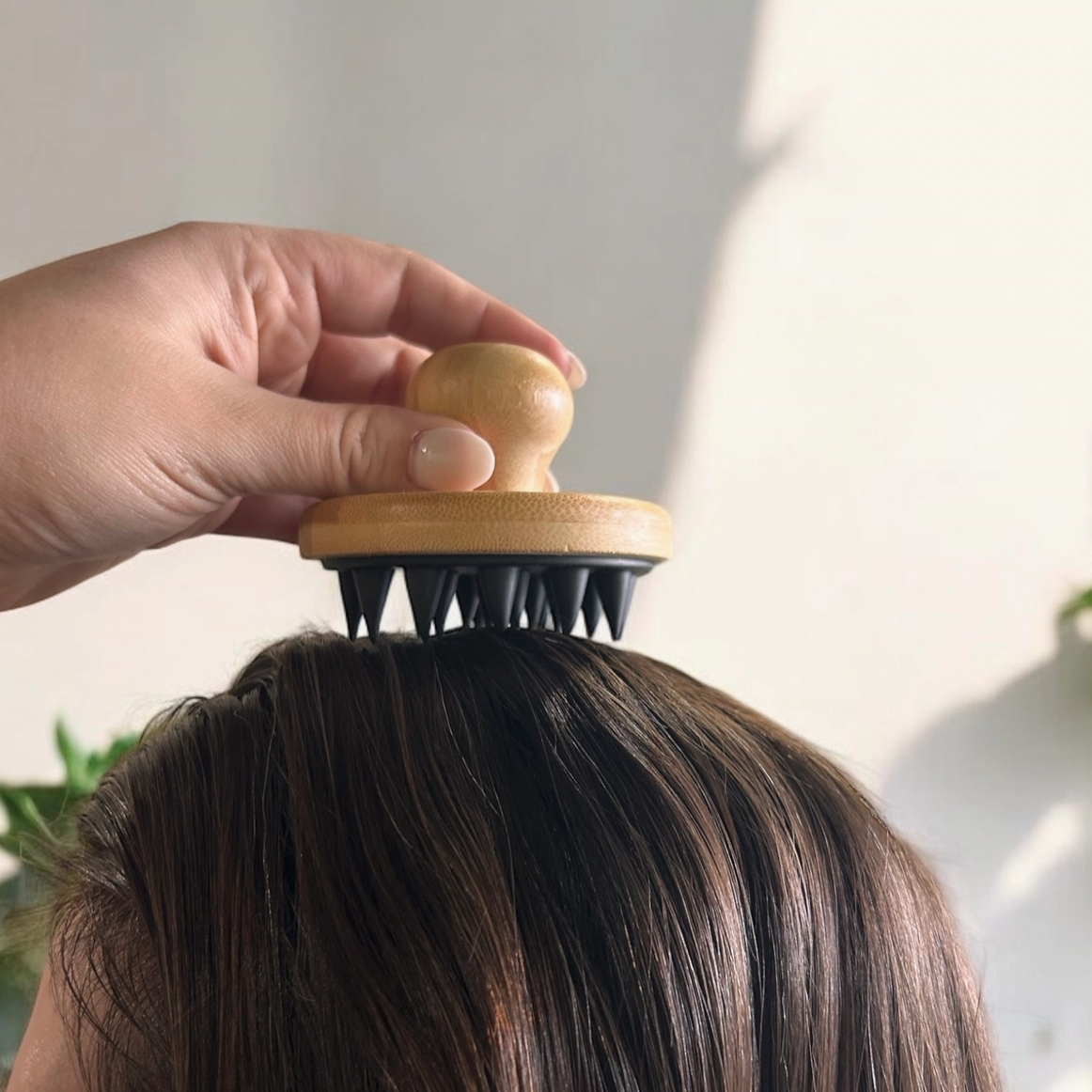 hand holding bamboo and silicone massager on head of brown hair