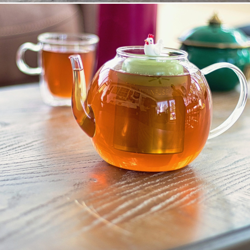 Teapot with a chicken-shaped tea infuser on a wooden table