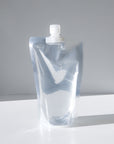 A clear, stand-up plastic pouch with a white screw cap filled with a floor cleaner sits on a white surface against a light gray background.