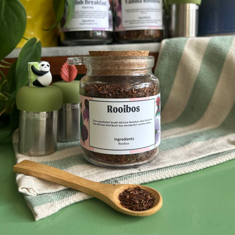 A refillable jar of Rooibos tea. The jar has a cork lid and an attachable bamboo spoon. 