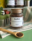 A refillable jar of Rooibos tea. The jar has a cork lid and an attachable bamboo spoon. 