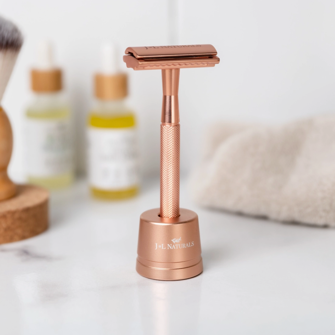 Rose gold safety razor on a white surface with blurred skincare products in the background