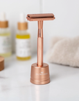 Rose gold safety razor on a white surface with blurred skincare products in the background