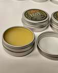 Open silver metal tins of Salud Salve showing the pale yellow salve inside, with one tin closed showing the round label with a sun and lavender, on a white background.
