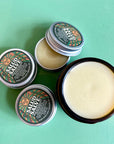 An open jar  and tin of salud salve showing the cream colored nourishing salve inside. 