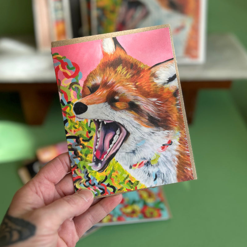 A hand holding a card featuring a high quality print of an oil painting of a fox with its jaw open in a yell. 