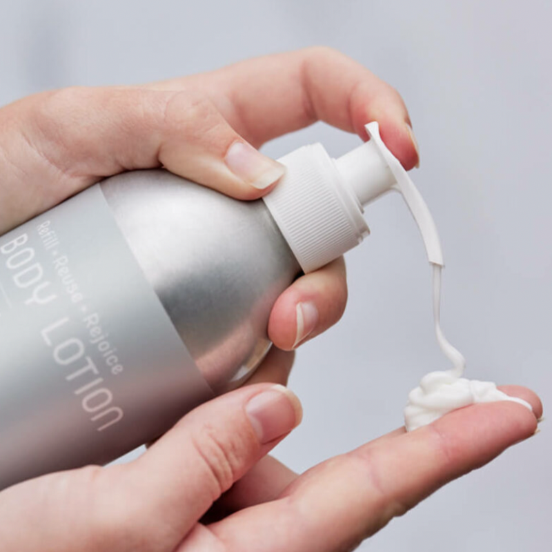 Someone dispenses Plaine Products Body Lotion from a silver, reusable bottle onto their hand.