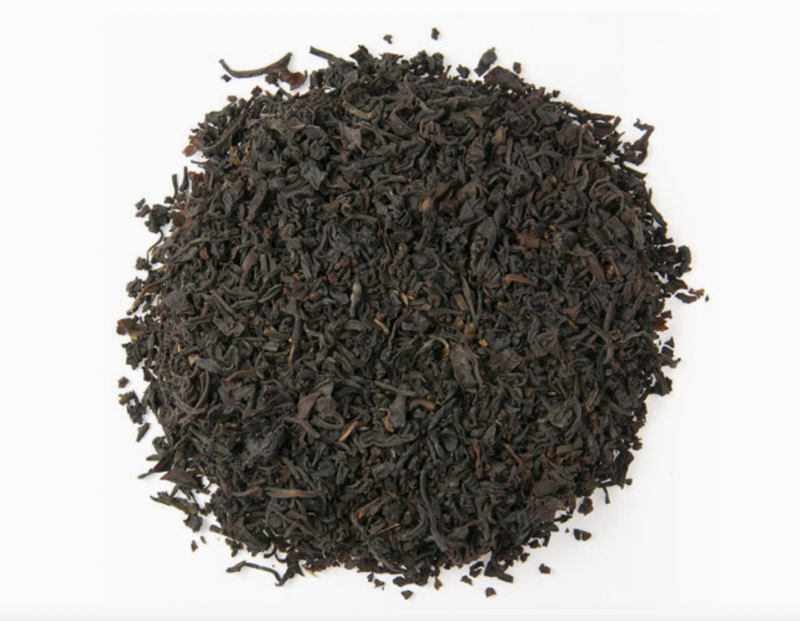 A pile of Loose Leaf Tea Co. English Breakfast tea is spread out on a white background, with dark, twisted leaves suggesting a full-bodied brew rich in flavor and aroma.
