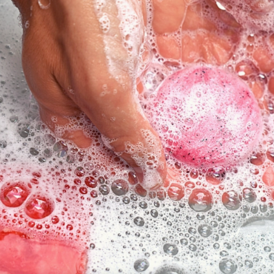 hands holding pink shampoo bar in bubbly water