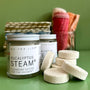 A Jar of refreshing shower steamers on a green background with a stack of shower steamers next to it. 