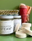 A Jar of refreshing shower steamers on a green background with a stack of shower steamers next to it. 