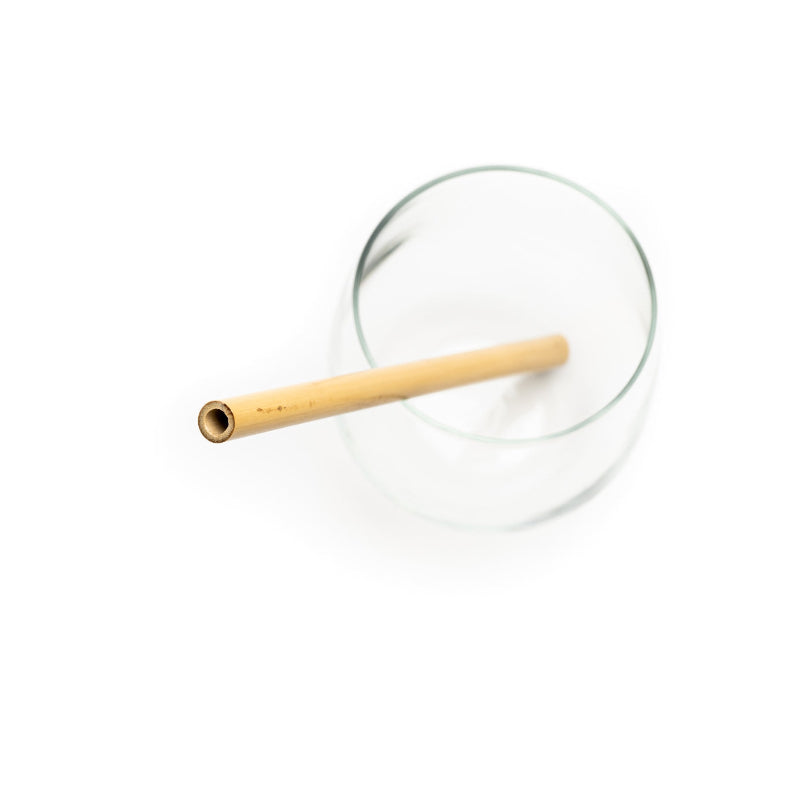 A glass with a reusable and compostable bamboo straw resting in it, on a white background. 