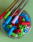A reused small glass jar full of multicolored reusable silicone straw tips.  Lying on the lip of jar are multicolored metal straws with silicone straw tips on them. 