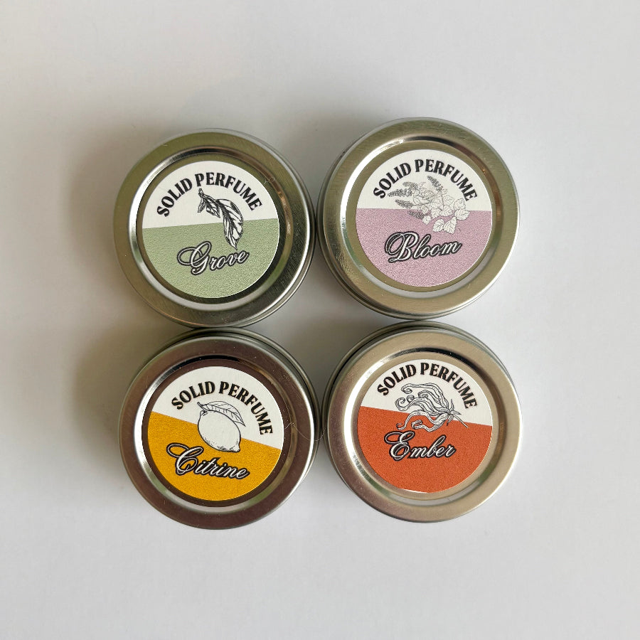 Four solid perfume tins with labeled lids on a light gray background