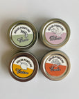 Four solid perfume tins with labeled lids on a light gray background
