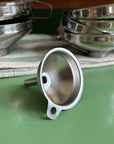 A small stainless steel funnel on a green tabletop with other larger stainless steel funnels in the background. 