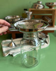 A hand holds a large stainless steel funnel over a large jar on a green table. 