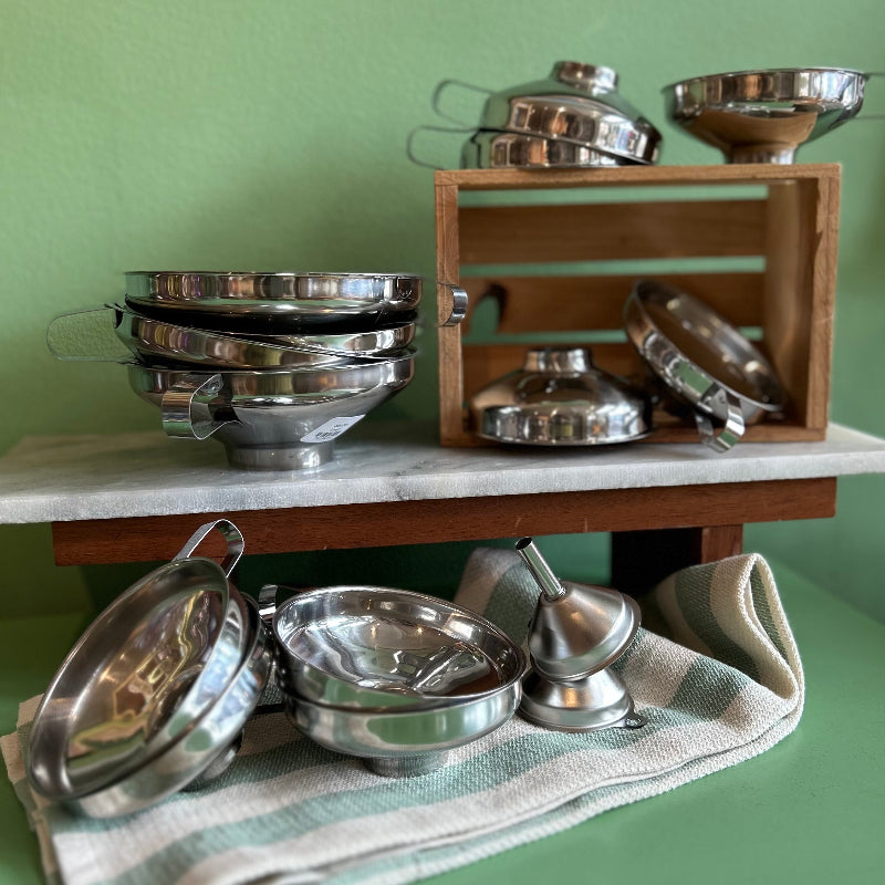 A large spread of different sized stainless steel funnels in stacks on a green background. 