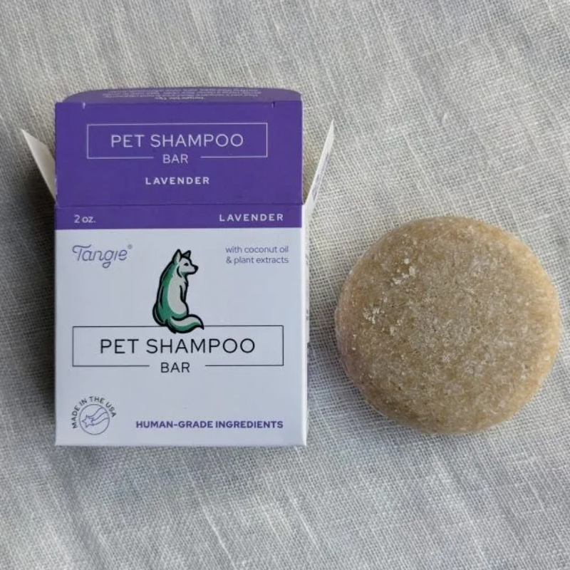 A purple Tangie Pet shampoo bar box with the shampoo bar in lavender next to it on a textured fabric background. 
