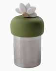 The Teany Tiny Kitchen Floating Tea Infuser features a cylindrical metal design with a green silicone lid and white lotus flower, providing an innovative and effortless way to steep your tea.
