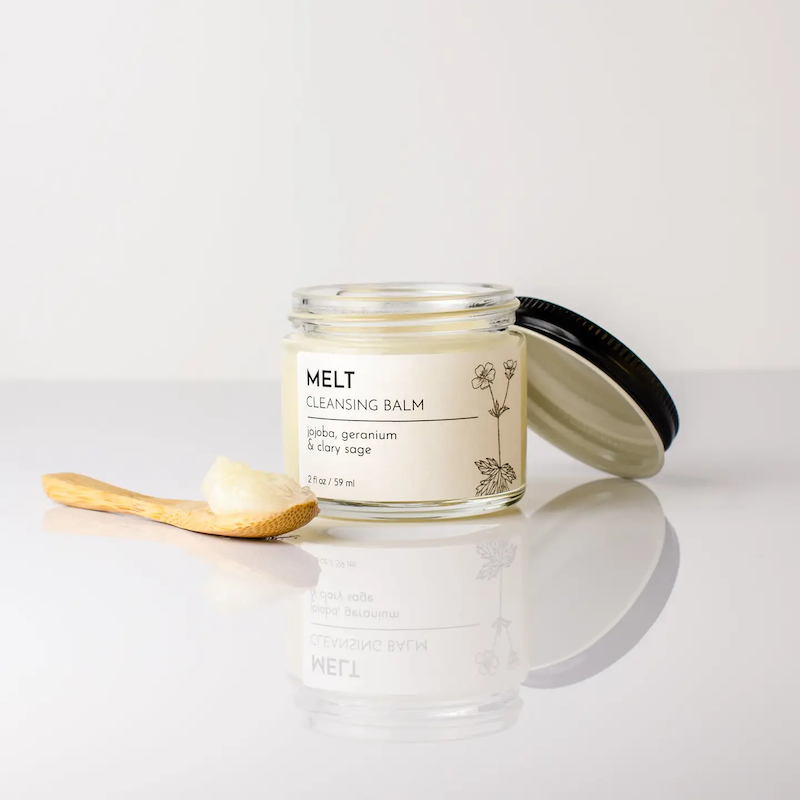 Glass jar of 'Melt' cleansing balm with a wooden spoon on a light background