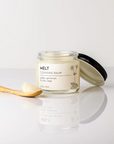 Glass jar of 'Melt' cleansing balm with a wooden spoon on a light background