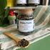 A refillable jar of white peony tea. The jar has a cork lid and an attachable bamboo spoon. The spoon is in front full of tea. 