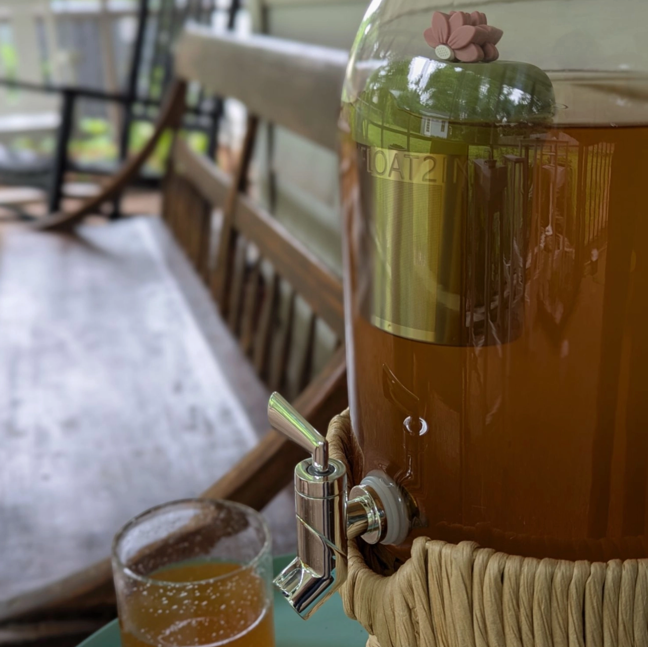 Brown drink dispenser with a glass of orange juice on a wooden table.