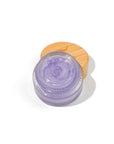 Small glass jar of the castor oil based plant based jelly in the flavor lavender lemonade. the jelly is a light purple with a shimmer to it. The jar has a bamboo lid and is on a white background.