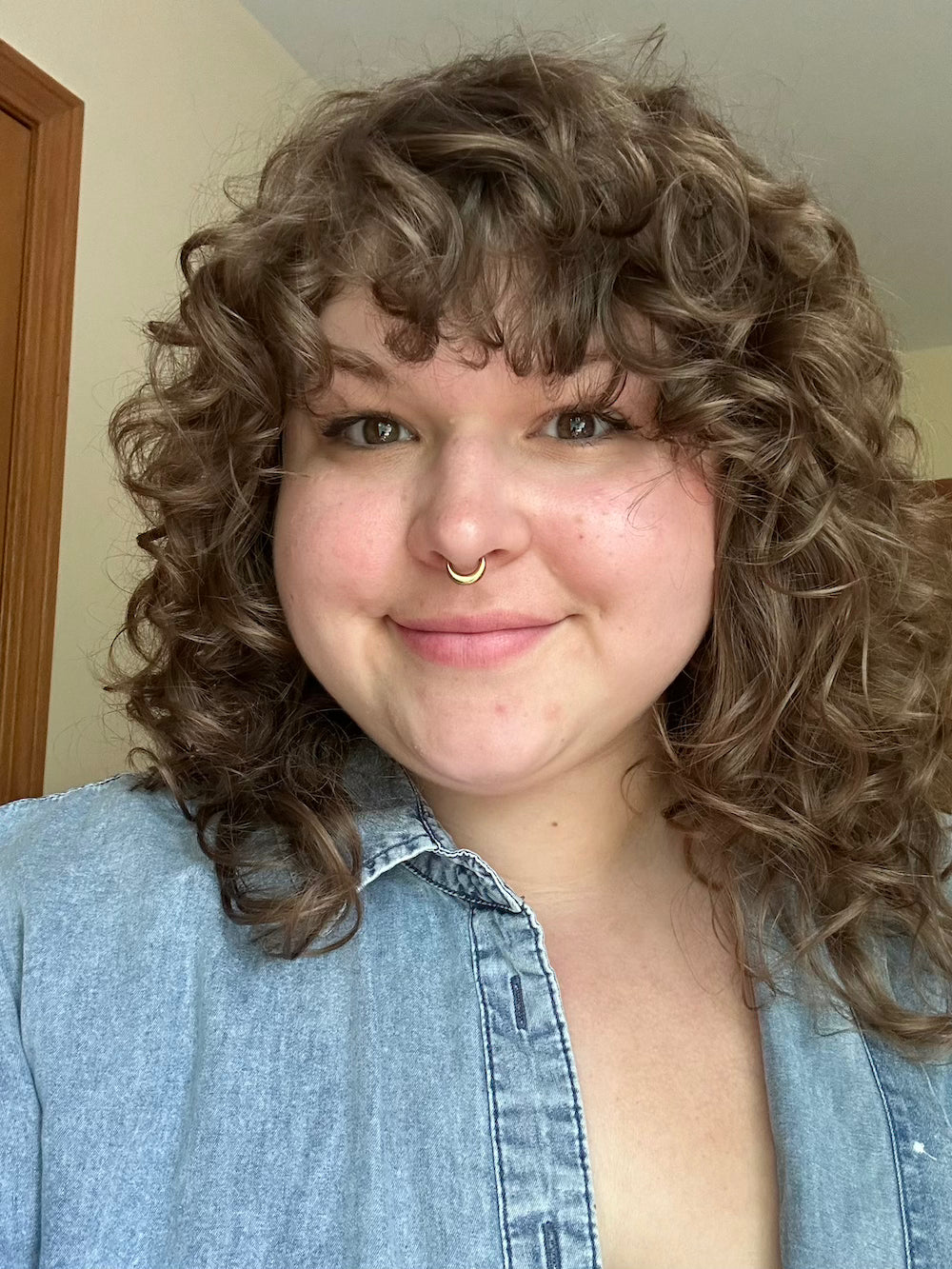 Person with curly hair wearing a blue denim shirt indoors.