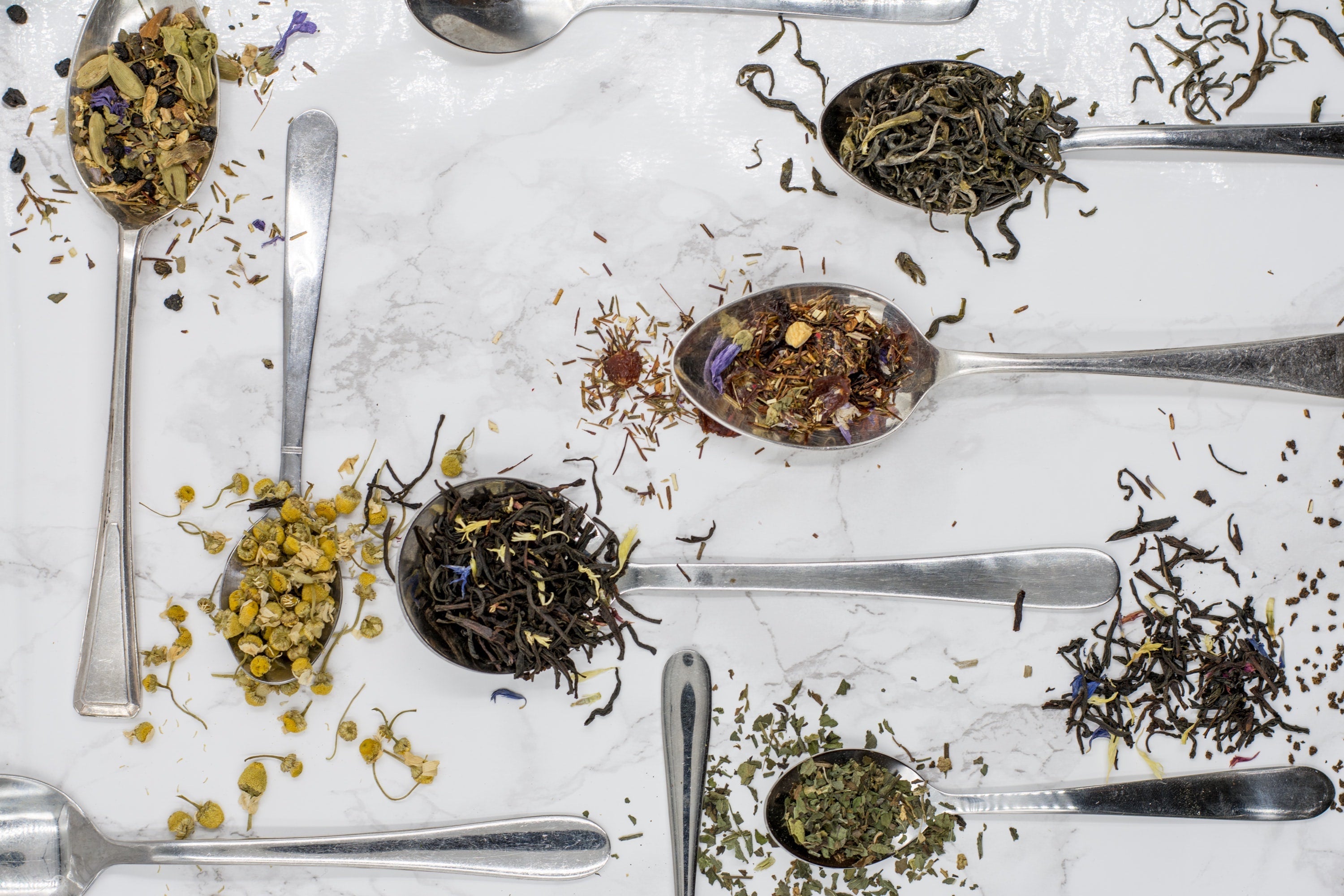White table with spoons filled with loose leaf tea 