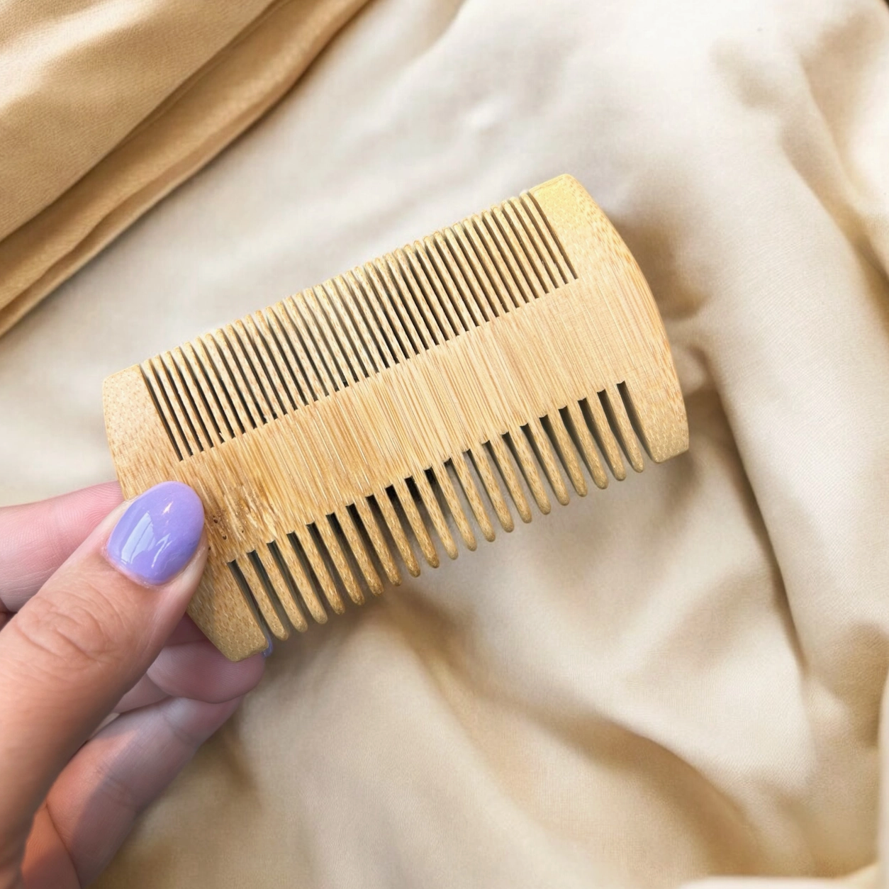 hand holding wooden comb on cream fabric. comb has wide tines on one side and narrow on the other. 