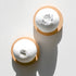 Two round white Cosh Bath Bombs with natural ingredients sit on circular wooden trays. One features a cluster of botanicals, while the other displays a subtle textured imprint, both casting shadows on a white surface.