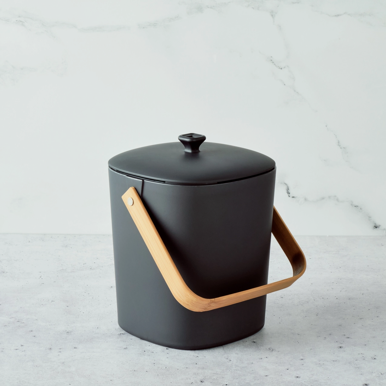 black container with wooden handle and lid on marble background