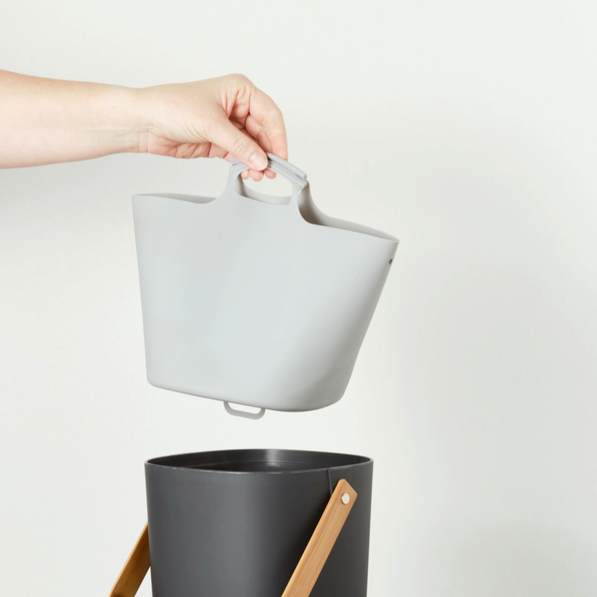 hand holding grey compost bin liner over black compost bin on white background 