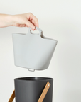 hand holding grey compost bin liner over black compost bin on white background 