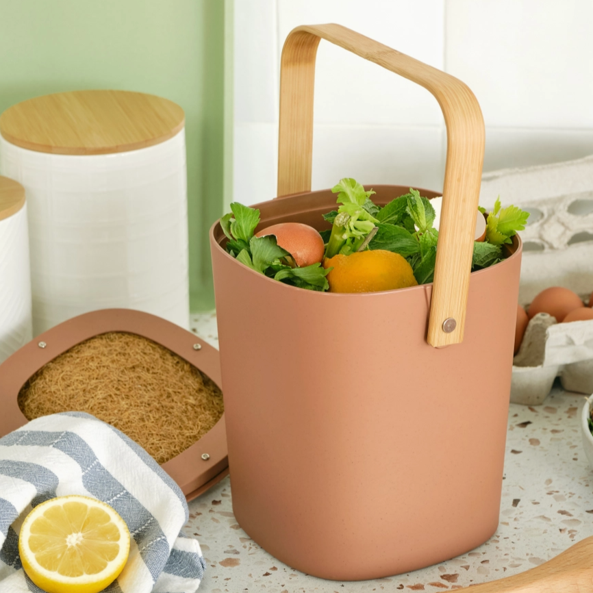 terracotta countertop compost bin filled with fruits on kitchen counter. 