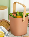 terracotta countertop compost bin filled with fruits on kitchen counter. 