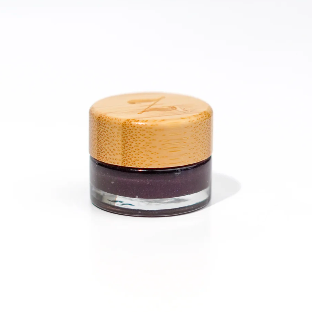 Small jar with a bamboo lid  filled with dark purple jelly on a white background