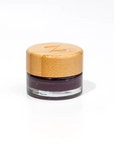 Small jar with a bamboo lid  filled with dark purple jelly on a white background