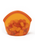 Small Amber Transparent silicone reusable snack bag holding sliced fruit on a white background. 