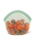 Small Green Transparent silicone reusable snack bag holding sliced tomatoes on a white background. 