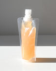 A clear refillable pouch holding orange gel face wash.