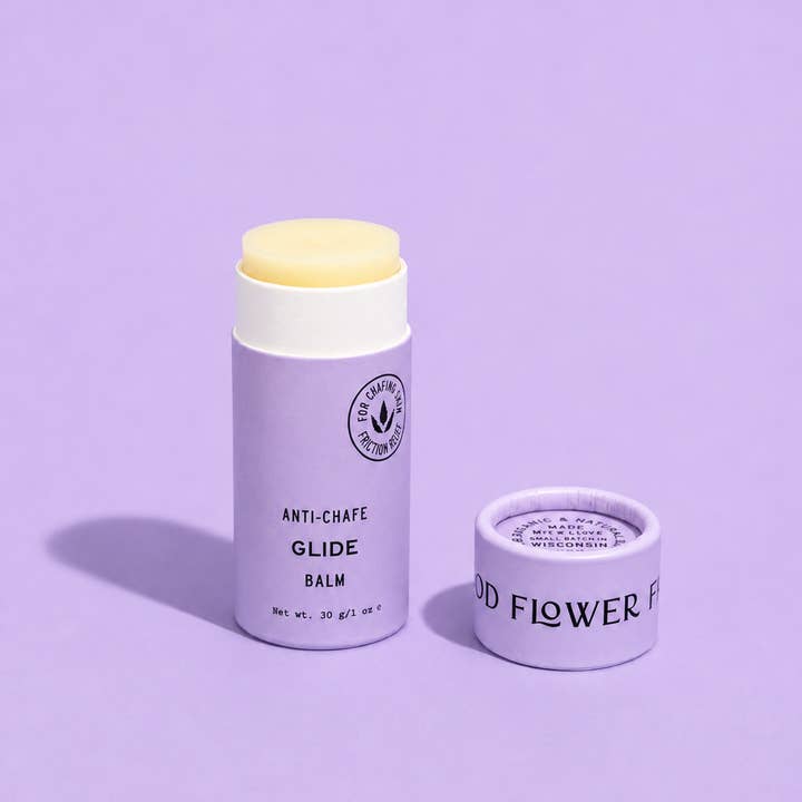 A lavender anti-chafe glide balm stick with a pale yellow balm visible at the top, shown next to its matching lavender cap on a solid lavender background.