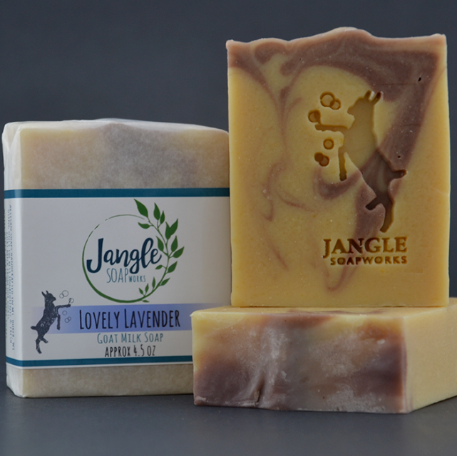 Jangle's Lovely Lavender Soap. The yellow swirled with purple bar is stamped with an image of a goat kicking bubbles. Two bars are unwrapped and one is upright on top of the other and the third bar is wrapped in paper. 