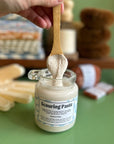A hand holds a bamboo spoon while it drizzles scouring scub into the jar. The fragrance free scrub is thick and ready to take on tough kitchen messes. 