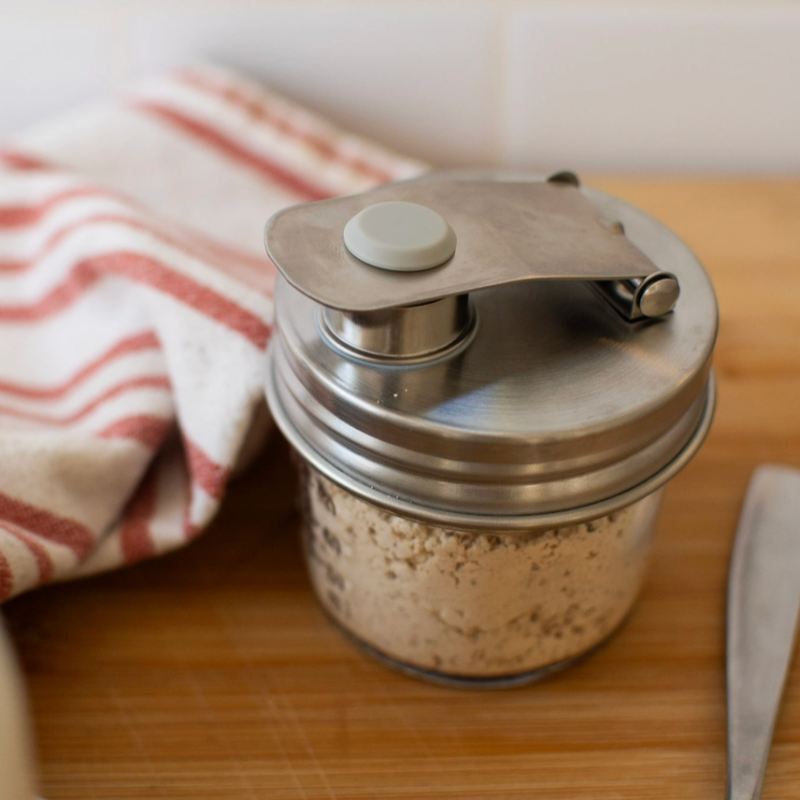 A stainless steel mason jar pour lid on jar filled with chopped onions, set on a wooden cutting board next to a striped kitchen towel.