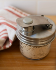 A stainless steel mason jar pour lid on jar filled with chopped onions, set on a wooden cutting board next to a striped kitchen towel.